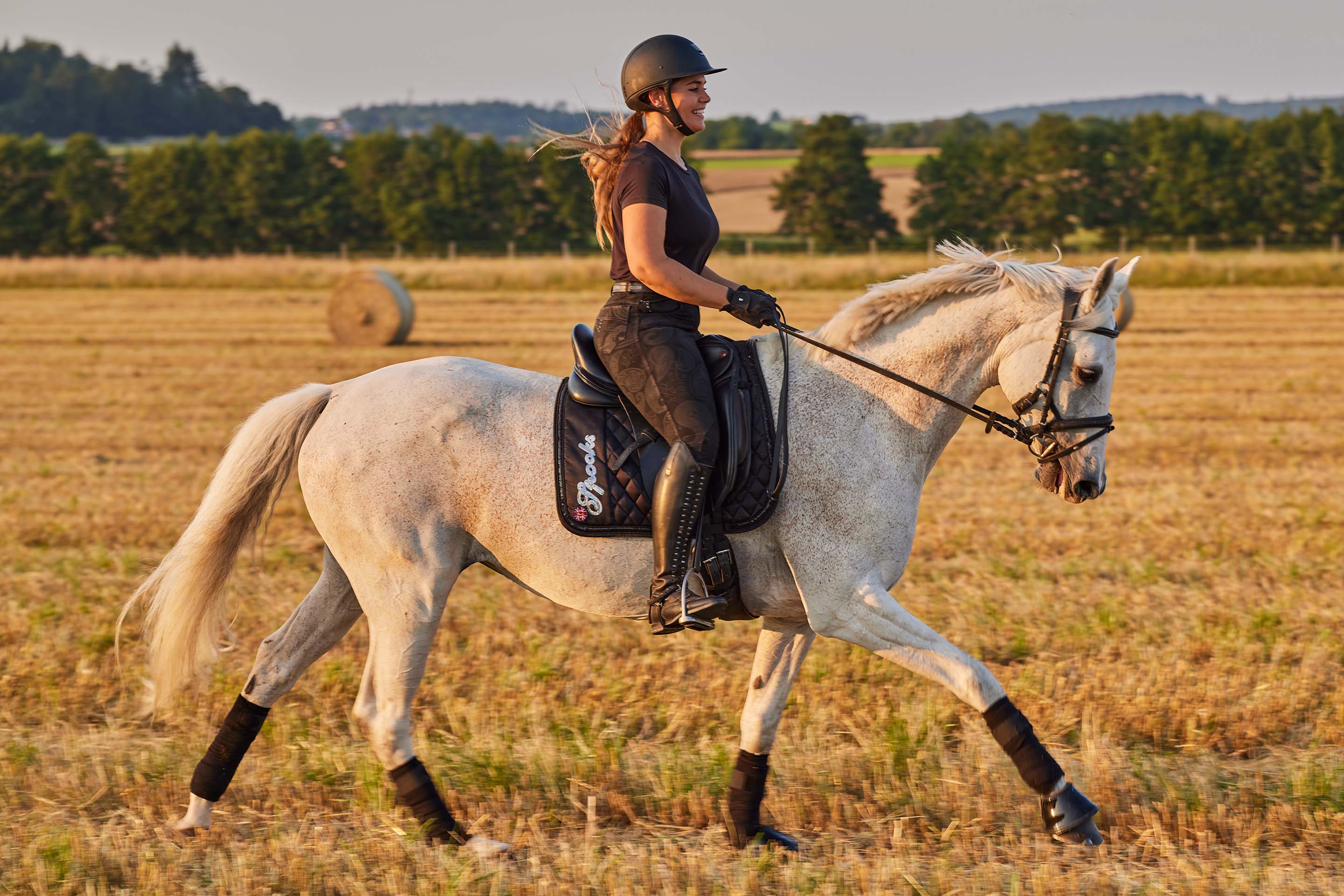Eine junge Frau reitet bei Sonnenuntergang auf einem weißen Pferd in einem Feld